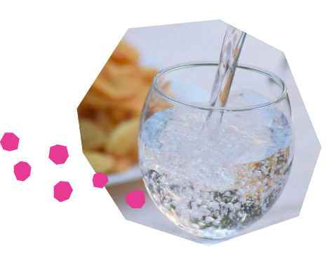 Un verre d'eau pétillante est rempli à partir d'une bouteille. À côté du verre, il y a une assiette de croustilles.