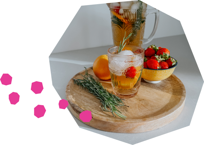 Un pichet rempli de cocktail gin-thé avec des oranges, des fraises et des concombres en brochette