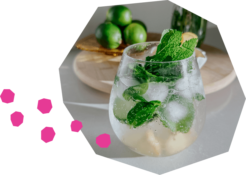 Un verre rempli du cocktail sans alcool Vert Vigueur avec du citron, des concombres et de la menthe autour du verre sur une table.
