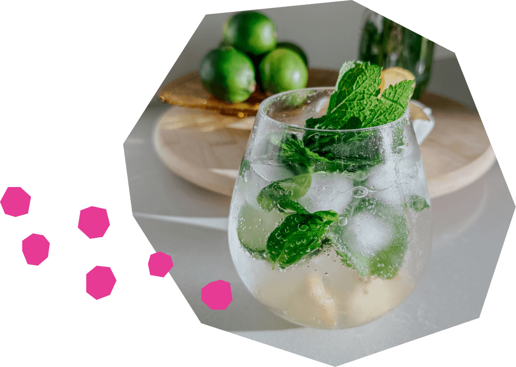 Un mocktail d'eau pétillante rafraîchissant dans un verre arrondi, rempli de glaçons, de tranches de citron vert et garni de feuilles de menthe fraîche.